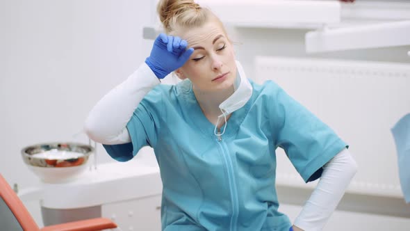 Medium Shot of Exhausted Dentist Sitting at Chair alt