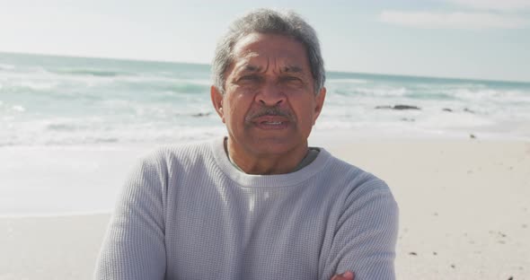 Portrait of hispanic senior man standing on beach and looking at camera