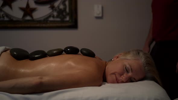 Medium shot of a mature caucasian topless woman with stones in a row down her back.  Woman has smile