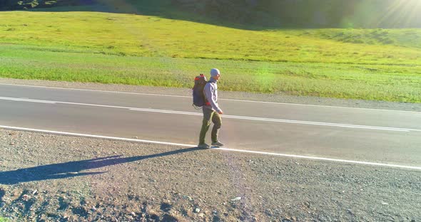 Flight Over Hitchhiker Tourist Walking on Asphalt Road. Huge Rural Valley at Summer Day. Backpack