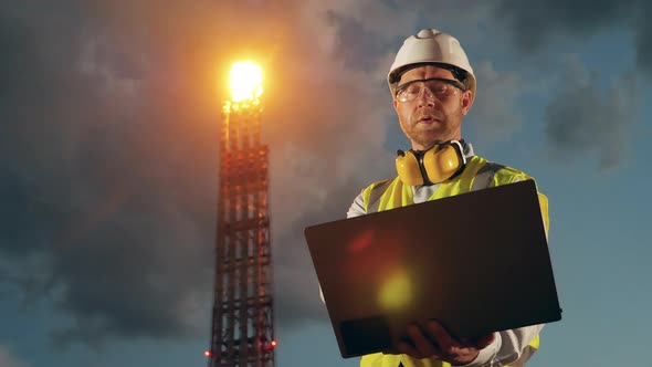 Male Worker with a Laptop Near the Oil Refinery Pipes