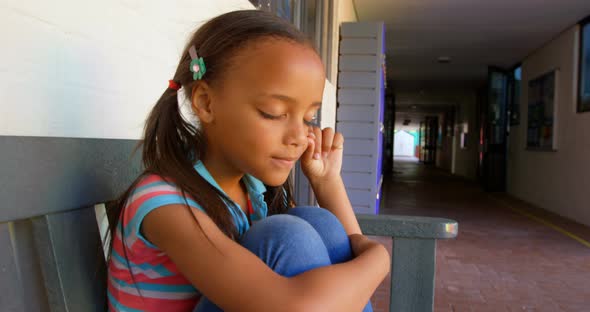 Side view of African American schoolgirl sitting on bench and crying in school corridor 4k