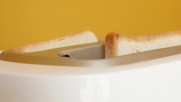 White two-slot automatic electric toaster in front of yellow background slow-mo footage