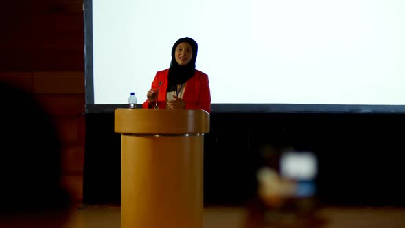 Mature Caucasian hijab businesswoman speaking at podium in auditorium 4k