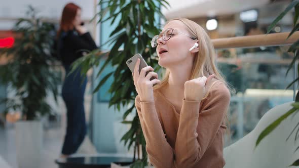 Caucasian Funny Blonde Girl Wears Wireless Headphones Listens to Music in Mobile Musical Application