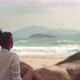 Young Woman Sits Near Rocks Looking at Sea on Wild Beach - VideoHive Item for Sale