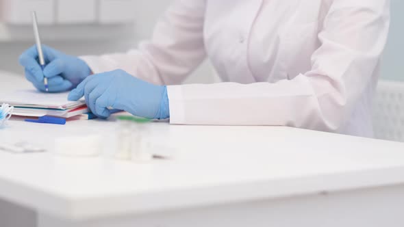 Unrecognizable Woman Doctor Surgeon in White Uniform is Writing Diagnosis and Examination Results