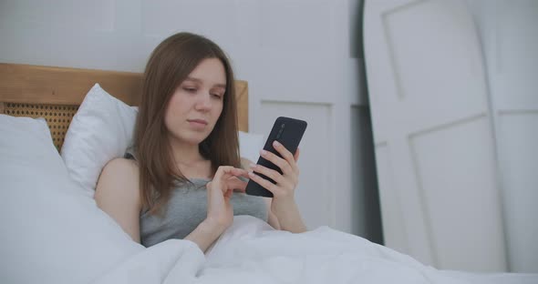 Woman in Morning Sitting in Bedroom Leaning Against the Soft Leather Back of Bed. Write Messages