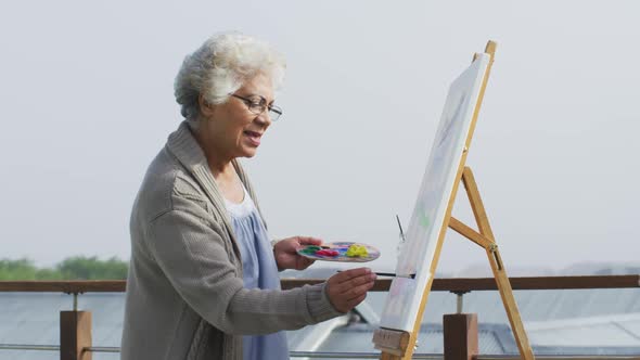 African american senior woman painting on canvas in the balcony at home