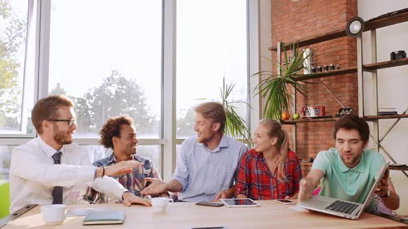 Five Interracial Friends Sitting at Table with Mobile Phones Tablets Laptop Speaking Smiling Giving