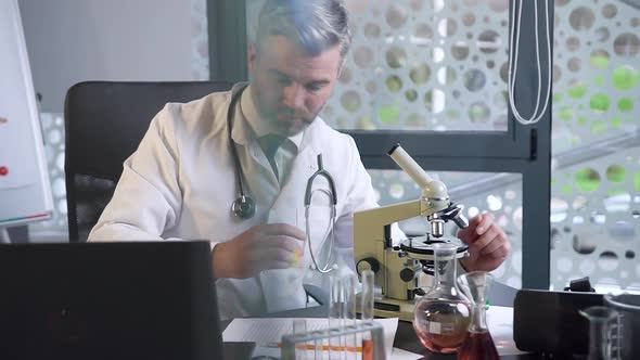 Male Doctor Which Working in the Clinic Lab, Looking Into Microscope and Typing the Datas