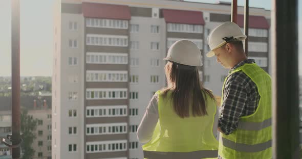 Back View Young Foreman and Engineer Checking the Blueprint and Talking About Construction Project