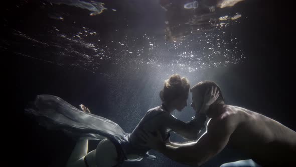 Lovers Underwater Beautiful Woman and Handsome Man are Floating in Darkness