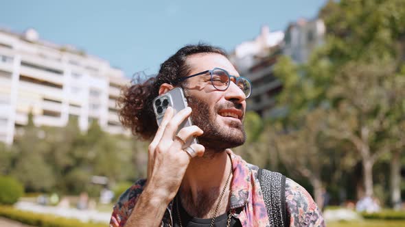 Sunny curly-haired bearded man in eyeglasses talking on phone