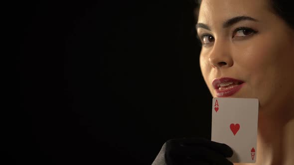 Flirty Lady Stroking Her Face With Ace of Hearts Card and Smiling to Camera