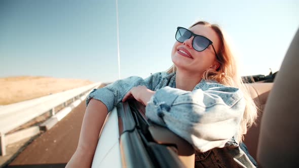 Happy young woman hang out of car window on sunny road trip day, enjoy views in outdoor