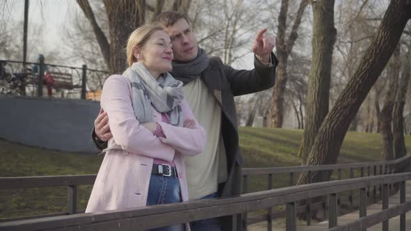 Portrait of Young Caucasian Man in Love Pointing Away and Talking To Older Woman. Happy Couple