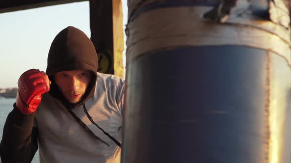 Boxer in red gloves trains blows on a punching bag in an abandoned building. Outdoor workout.