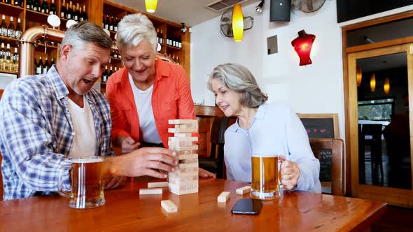 Senior friends toasting glass of beer while playing jenga 