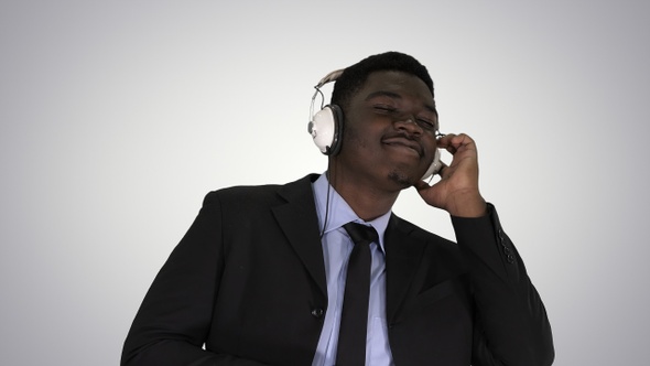 Black businessman dancing to music in headphones on gradient