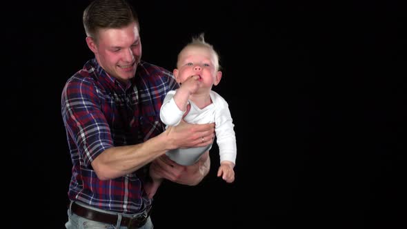 Affectionate Father Playing with Baby Son at Home - Lifting Him Up and Making Him Laugh. Black