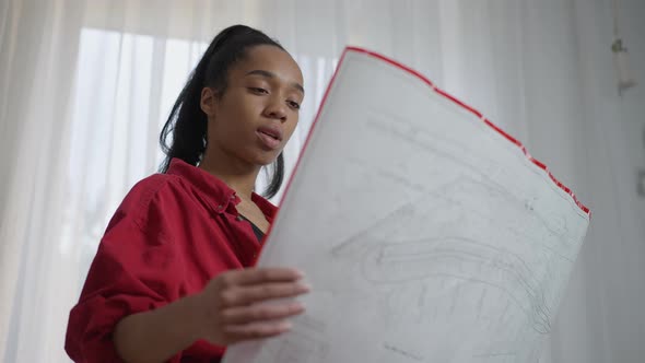 Thoughtful African American Young Woman Holding Blueprint in Hands Planning Architectural Project