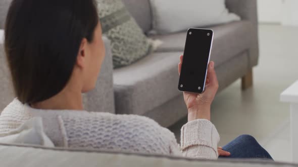 Back view of asian woman sitting on sofa, resting with smartphone with copy space at home