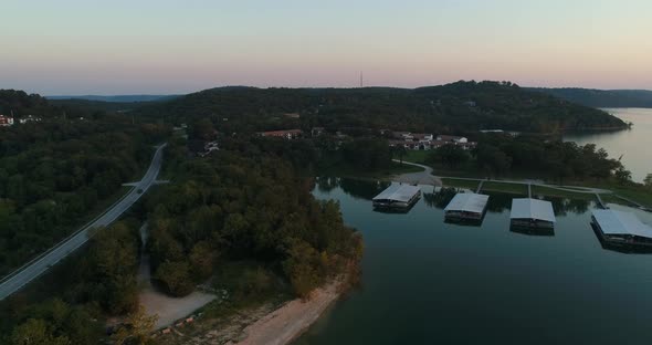 Aerial view over a lake marina and flying sideways to show a road through forested area