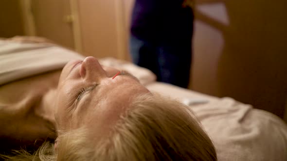 Detail of an acupuncture needle in the forehead of a caucasian woman at a spa. Woman is talking with