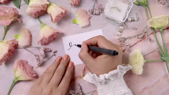 Hands writing RSVP on a card near pink flowers close up on a marble table