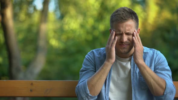 Man Massaging Temple on Bench at Park, Suffering From Migraine Pain, Health