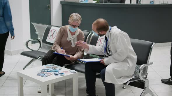 Physician and Senior Woman with Face Masks Talking in Waiting Area