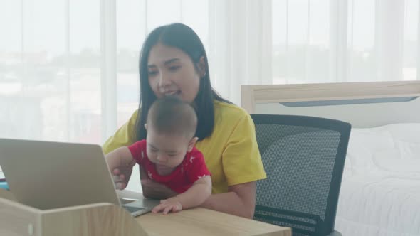 Happy family with mother carrying baby and working on laptop computer to internet online at home.