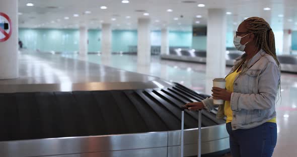 African senior woman waiting for luggage on the airport while holding coffee cup