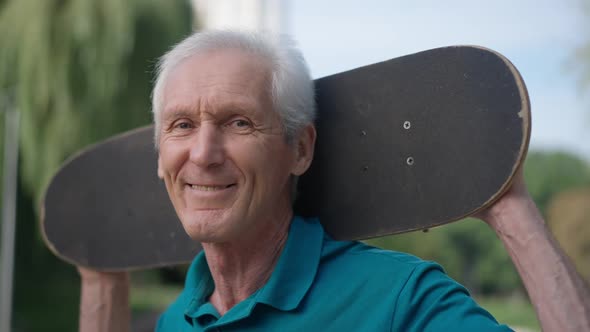 Closeup Portrait of Happy Smiling Senior Sportsman with Skateboard on Shoulders Looking at Camera