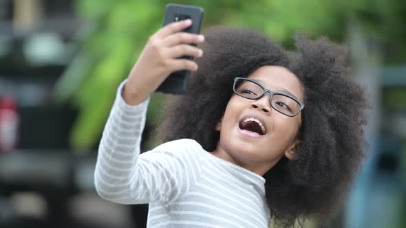 Young Cute African Girl with Afro Hair Video Calling with Phone in the Streets Outdoors