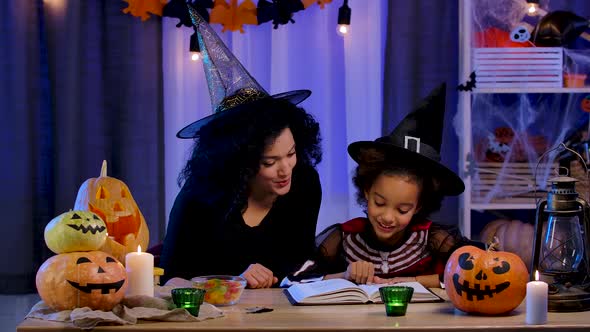 Little African American Girl in Festive Costume and Witch Hat Read Book