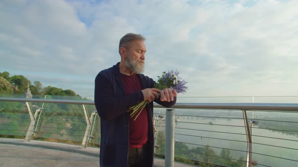 Senior Bearded Man with Bouquet of Flowers Waiting for Spouse