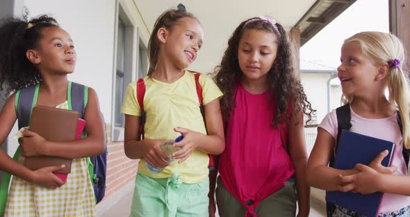 Video of happy diverse girls walking at school corridor and talking