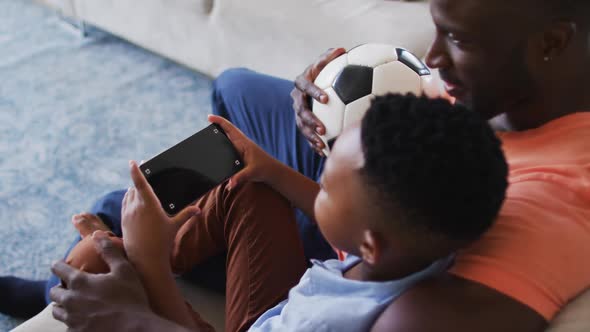 African american father and son using smartphone with copy space while sitting on the couch at home