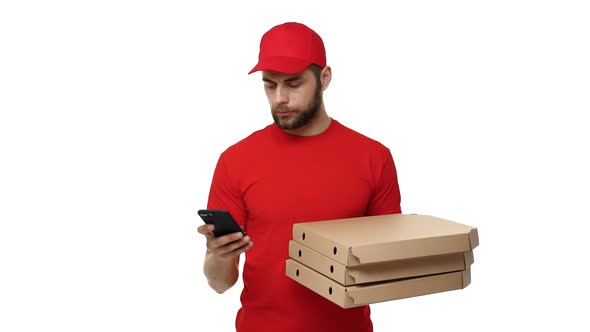 Delivery Boy in a Red Uniform Holding a Stack of Pizza Boxes and Checking Order on Mobile Phone