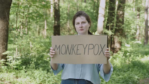 Plus Size Young Woman Stands with Cardboard Poster Saying Monkeypox in Forest