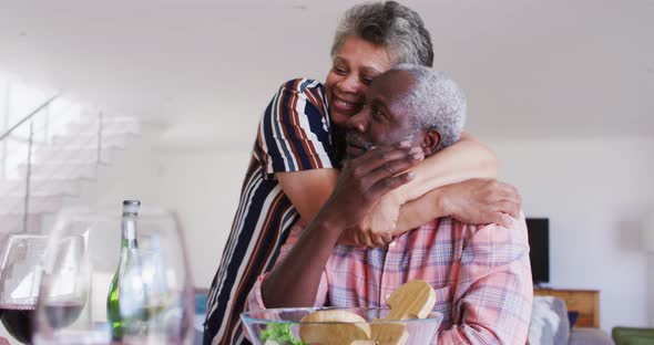 African american senior couple sitting by a table drinking wine eating dinner and hugging