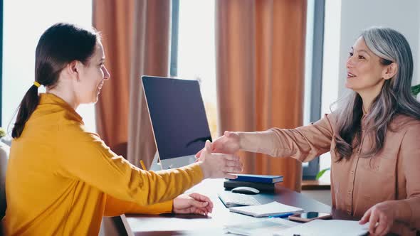 Two Smiling Women Shaking Hands Indoors Office