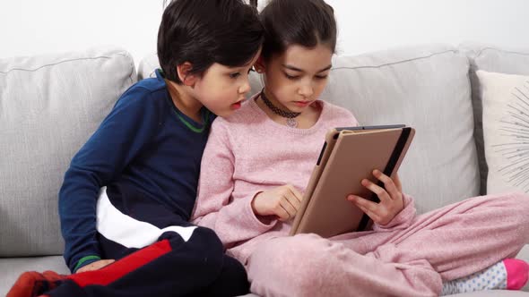 Two Mixedrace Kids Sitting on Sofa with Tablet