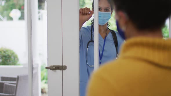 Mixed race female doctor wearing face mask knocking on doors at home