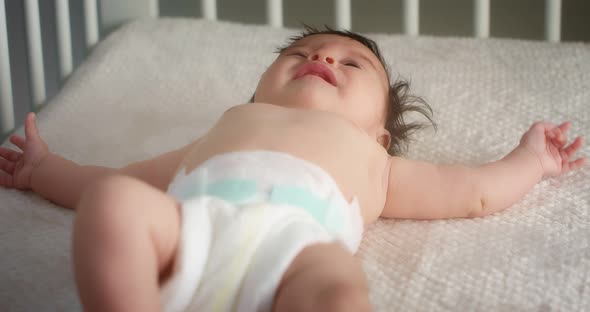 Newborn Baby in a Diaper Lies on Its Back in a Light Child Crib