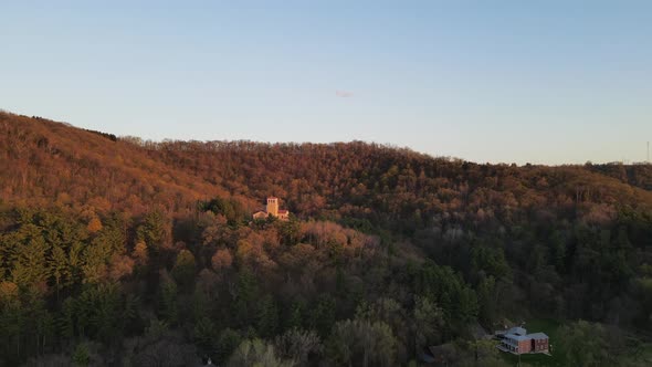 Aerial view around forest covered mountain at sunset with religious shrine tucked into trees.