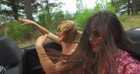 Two carefree girls partying while riding in cabriolet