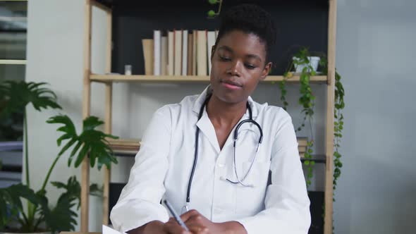 Portrait of african american female doctor having a video chat listening and writing notes